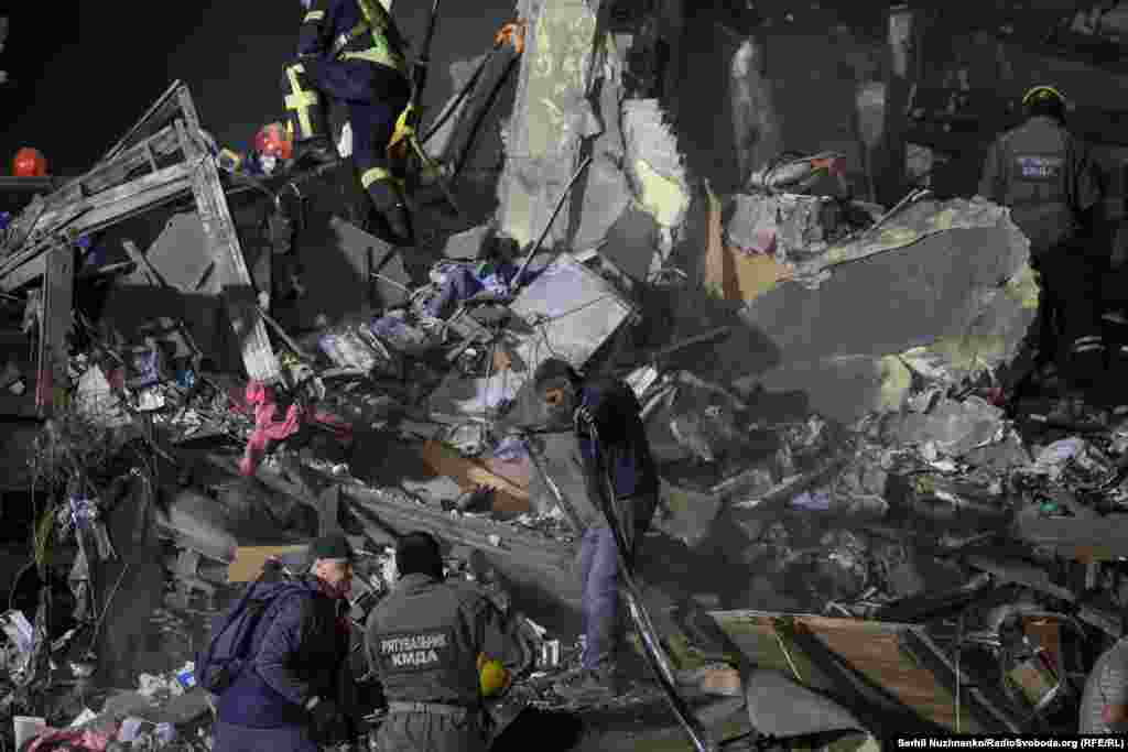 Rescuers work at the site of an apartment building hit by a Russian ballistic missile in Kyiv.Rescuers rushed to pull survivors from building debris, listening for mobile phones ringing to try and locate people.